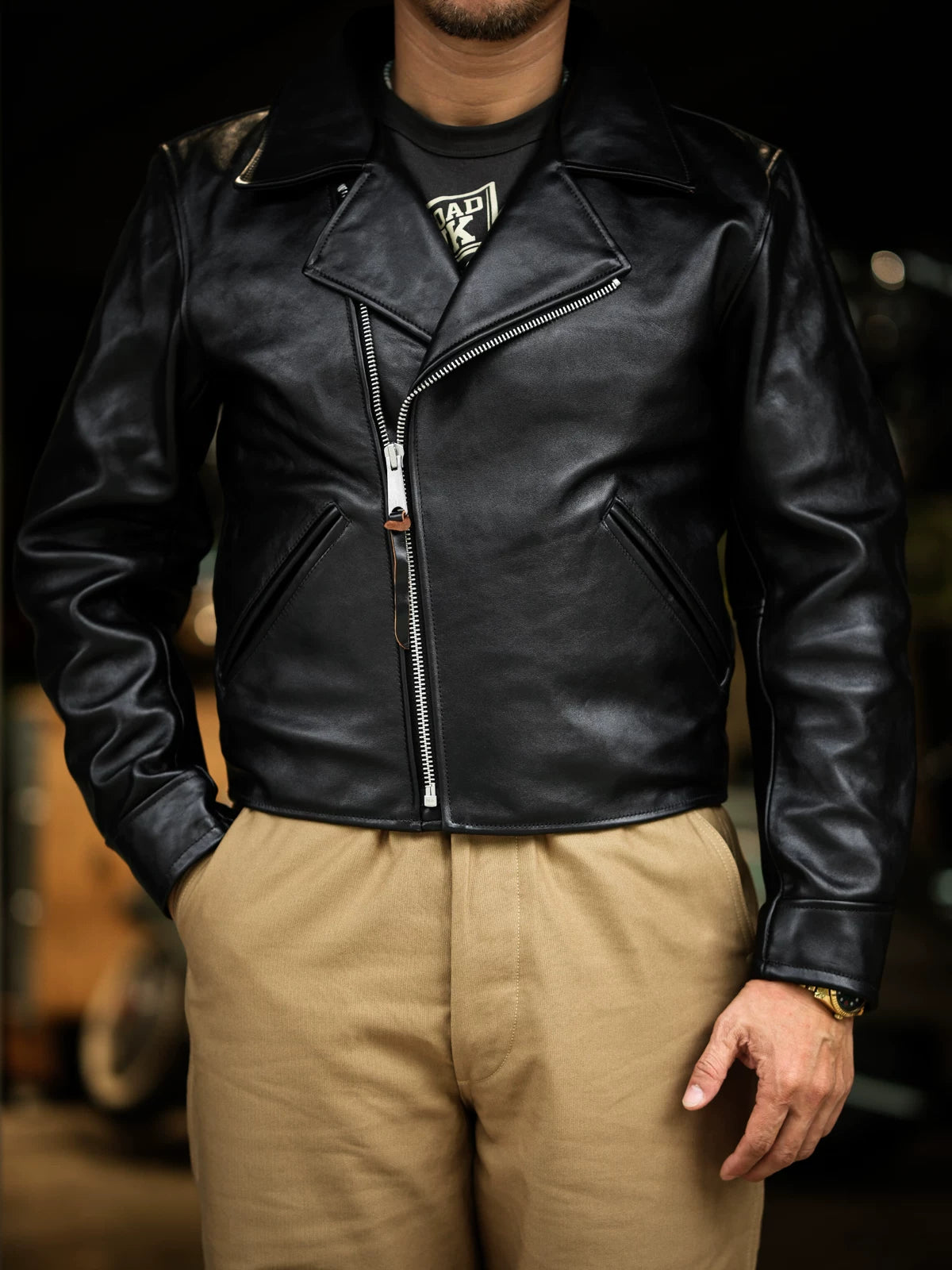 Black tea-core horsehide Nuremberg jacket worn zipped front, hands in pockets, boxy 1940s silhouette