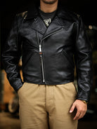 Black tea-core horsehide Nuremberg jacket worn zipped front, hands in pockets, boxy 1940s silhouette