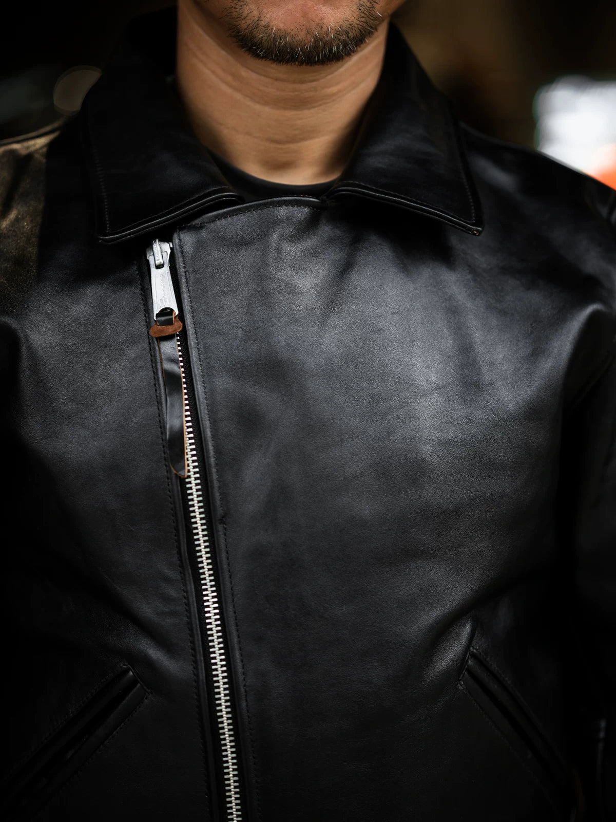 Close-up of diagonal antique metal zipper and wide lapel on black tea-core horsehide